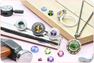 Jewelry-making tools and colorful gemstones on a table, with rings and a pendant necklace displayed.