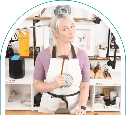 Person with light hair holding a hammer in a jewelry making workshop, surrounded by jewelry making tools.  From a Jewelry making blog.