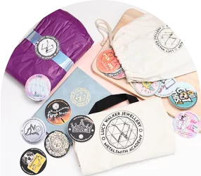 Assorted jewelry academy badges, a cloth pouch, and wrapped items with "Lucy Walker Jewelry" logo displayed.
