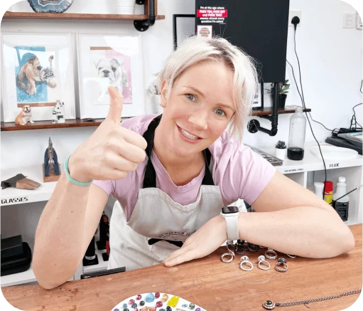 Person smiling and giving a thumbs-up at a table with jewelry making items.