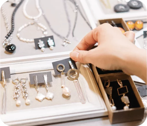A hand selecting jewelry from a display of assorted earrings and necklaces.