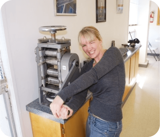 Smiling woman using a rolling mill in a jewelers workshop.