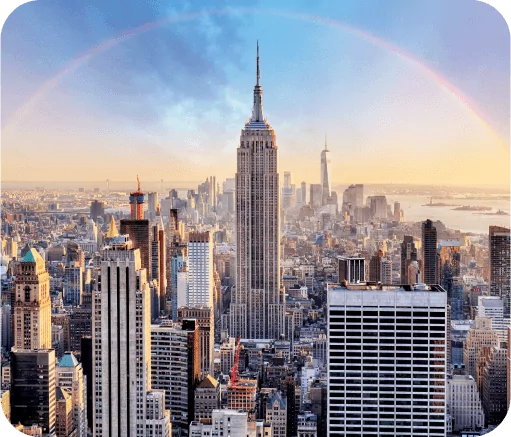 Aerial view of a city skyline with a prominent skyscraper and a faint rainbow in a clear sky.