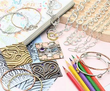Jewelry and art supplies on a table, including bracelets, necklaces, colored pencils, and an open book.