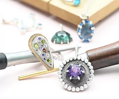 Assorted jewelry pieces with gemstones, including a purple pendant, displayed with crafting tools.
