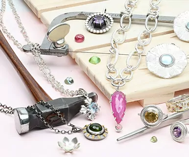 Jewelry-making tools and materials, including chains, gemstones, and a pink gemstone pendant, on a wooden surface.