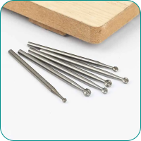 Six small metal engraving burrs on a surface, with a wooden block in the background.