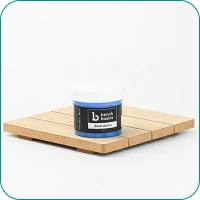 A jar of black shea butter on a wooden platform against a plain background.