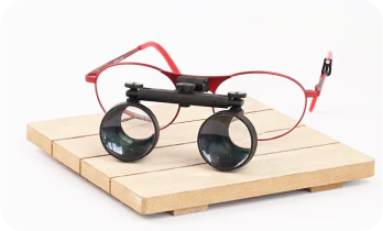 Red-framed glasses with attached binocular lenses on wooden surface.