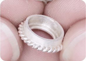 Close-up of a hand holding a textured silver ring with a twisted rope design along its outer edge. From a class on how to make a ring with beaded wire.