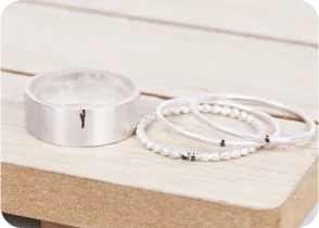 Three silver rings arranged on a wooden surface. One is wide, and two are thin with beads. From a class on how to make a ring with beaded wire.