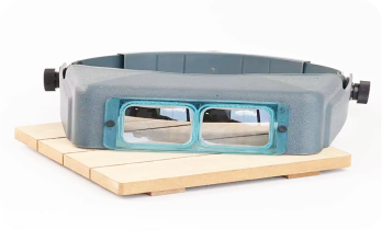 Gray headband magnifier with lenses, resting on a wooden platform.