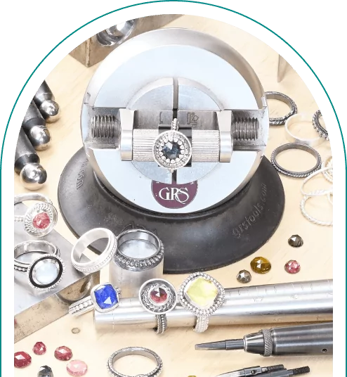 Jewelry-making tools with rings, gemstones, and a vise on a wooden surface.