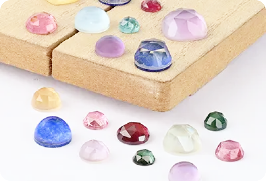 Assorted colorful gemstones on a wooden surface, including blue, red, green, and pink stones.