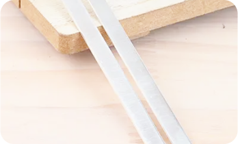 Silver chopsticks and a wooden board on a light surface.