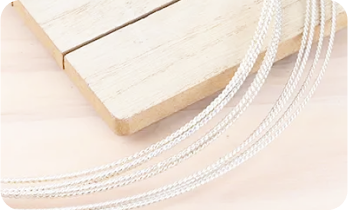 Close-up of a wooden board with several braided silver cords draped over it.