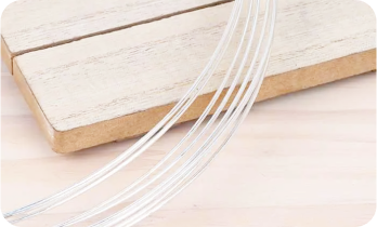 Coiled silver wires resting on a wooden board with a light background.