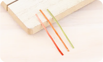 Three thin strips in red, orange, and green on a light wooden surface.