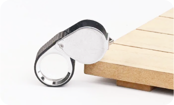 A magnifying glass loupe with a metal cover sits on a wooden surface.