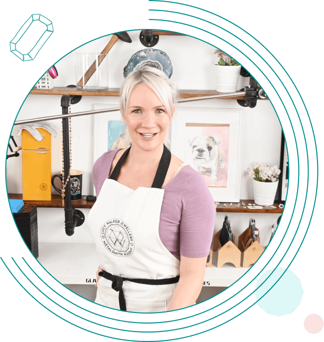 Person in a studio wearing an apron, standing in front of art supplies and framed pictures, smiling at the camera.