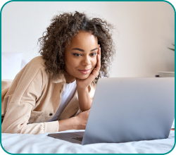 Woman lying on bed, looking at a laptop with a slight smile, in a relaxed home setting.