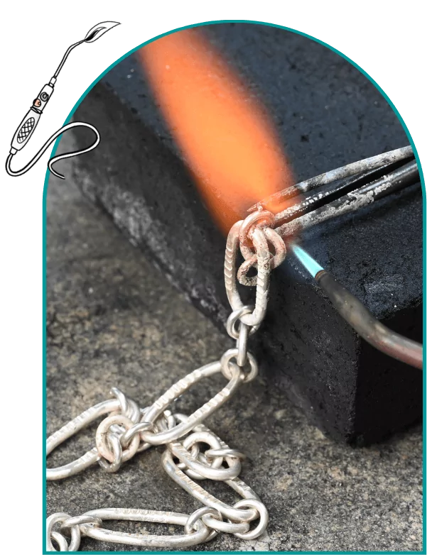 Close-up of a silver chain link being soldered with a flame against a black block.  From a class on chain making and soldering silver.