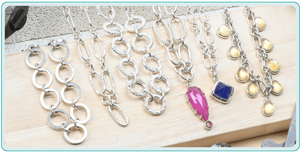Silver necklaces with various chain links and colorful gemstone pendants arranged on a wooden surface.  From a class on chain making and soldering silver.