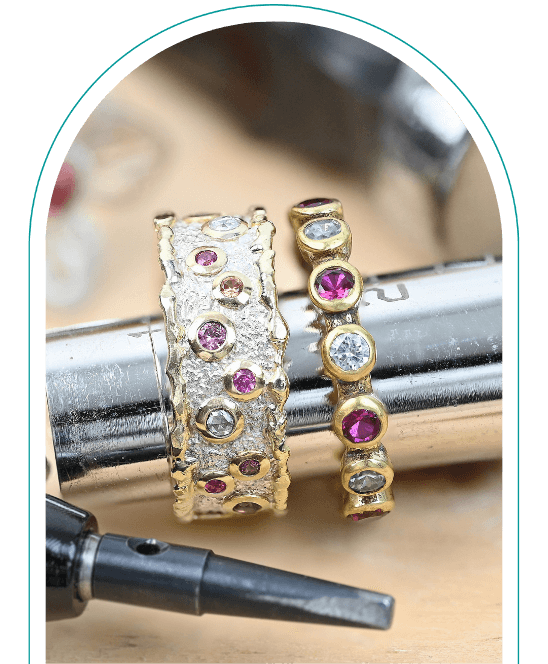 Two gold rings with red and clear gems placed on a metal tool, next to a black tool tip. From a class focusing on soldering gold.