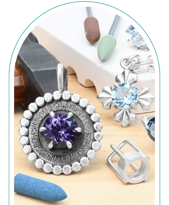 Jewelry-making tools and silver pendants with purple and blue gemstones on a wooden surface.  From a class on how to prong set round stones.