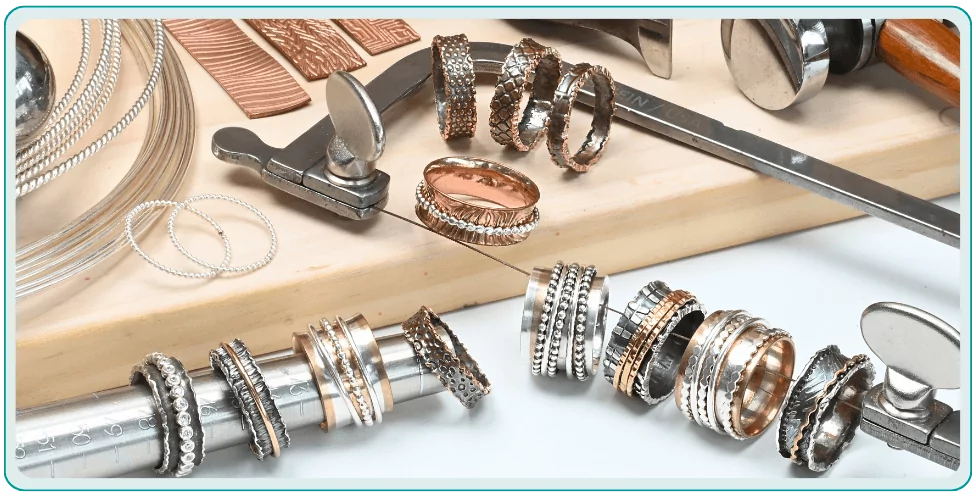 Assorted metal rings and jewelry-making tools arranged on a surface, including a mandrel and wires.  From a class on how to make a spinner ring