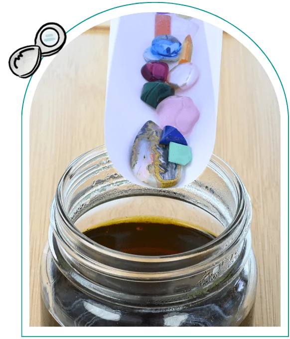 A jar with gemstones held over a jar with dark liquid on a wooden surface.  From a guide on how to use liver of sulfur