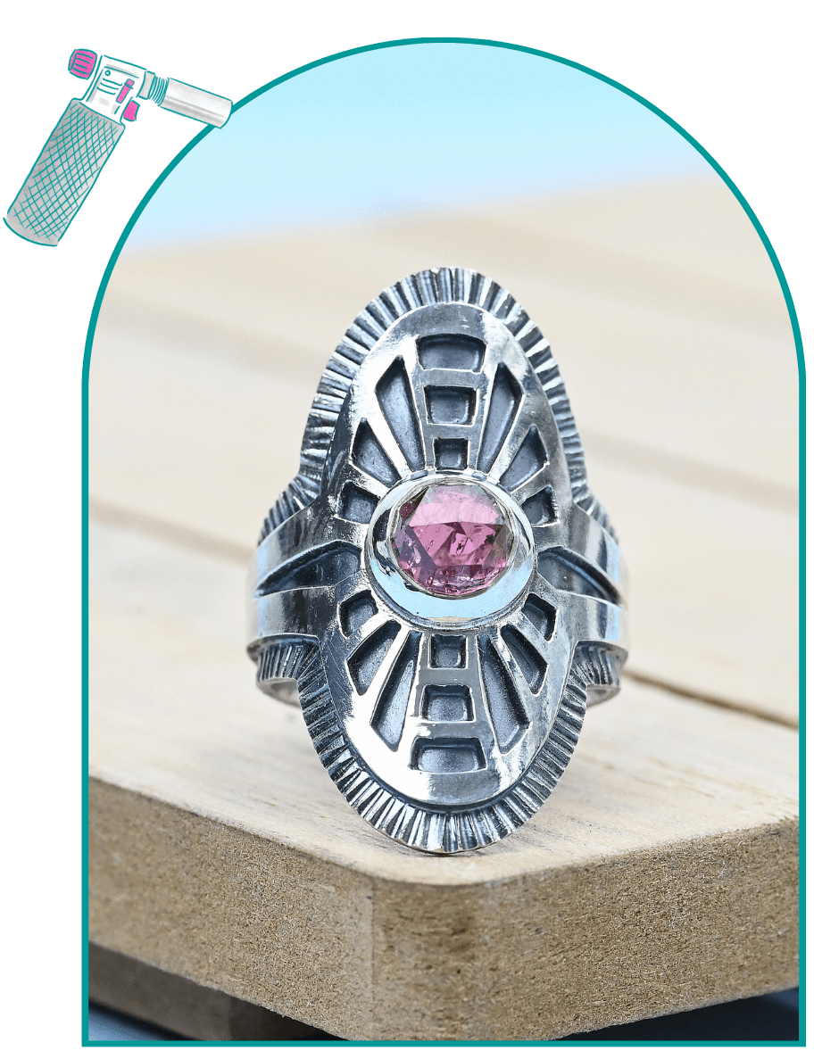 Silver ring with pink gemstone on a wooden surface, featuring intricate geometric design from a guide on how to make a saddle ring.