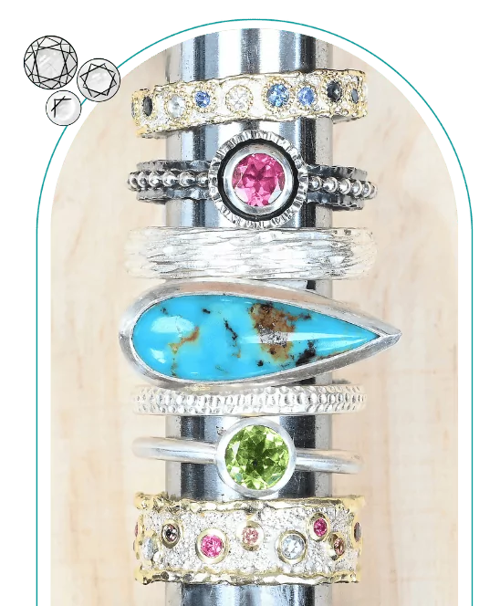 Stacked rings with various gemstones, including turquoise, pink, blue, and green stones, on a display rod. From a class on how to design jewelry.