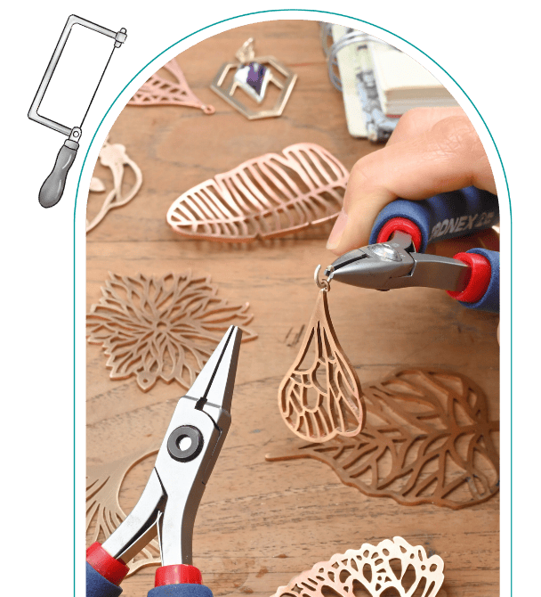 Person crafting intricate metal jewelry pieces with pliers on a wooden table. From a class on how to use a jewelers saw.